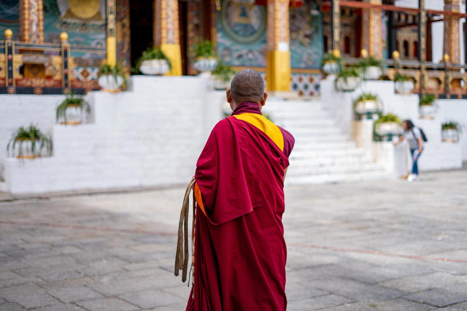 A Buddhist monk in traditional attire walks towards a Bhutanese temple, capturing the serene essence of religious devotion