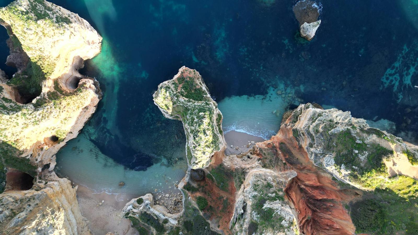 Aerial view of a rocky cove with rust-red cliffs and turquoise water