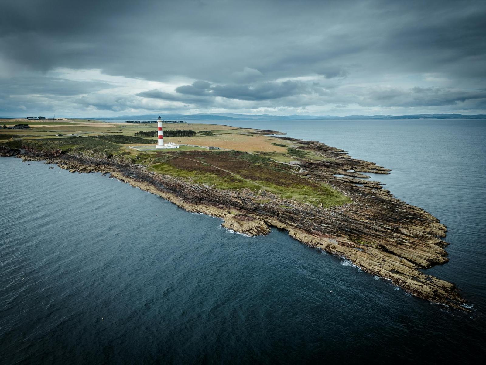 A striped lighthouse on a rocky headland jutting into the sea