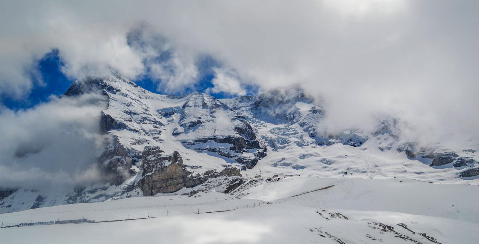 Breathtaking landscape of clouds in rocky mountains with snow and road on slope