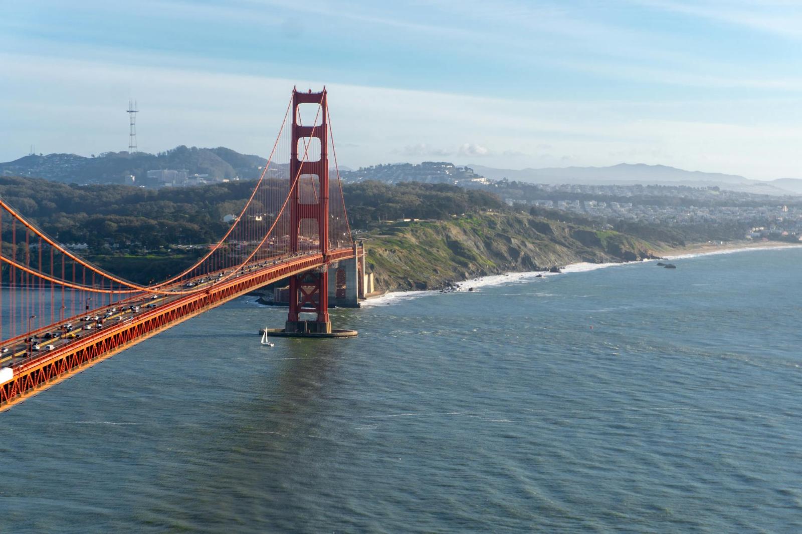 A red suspension bridge spanning a bay beside a coastal headland