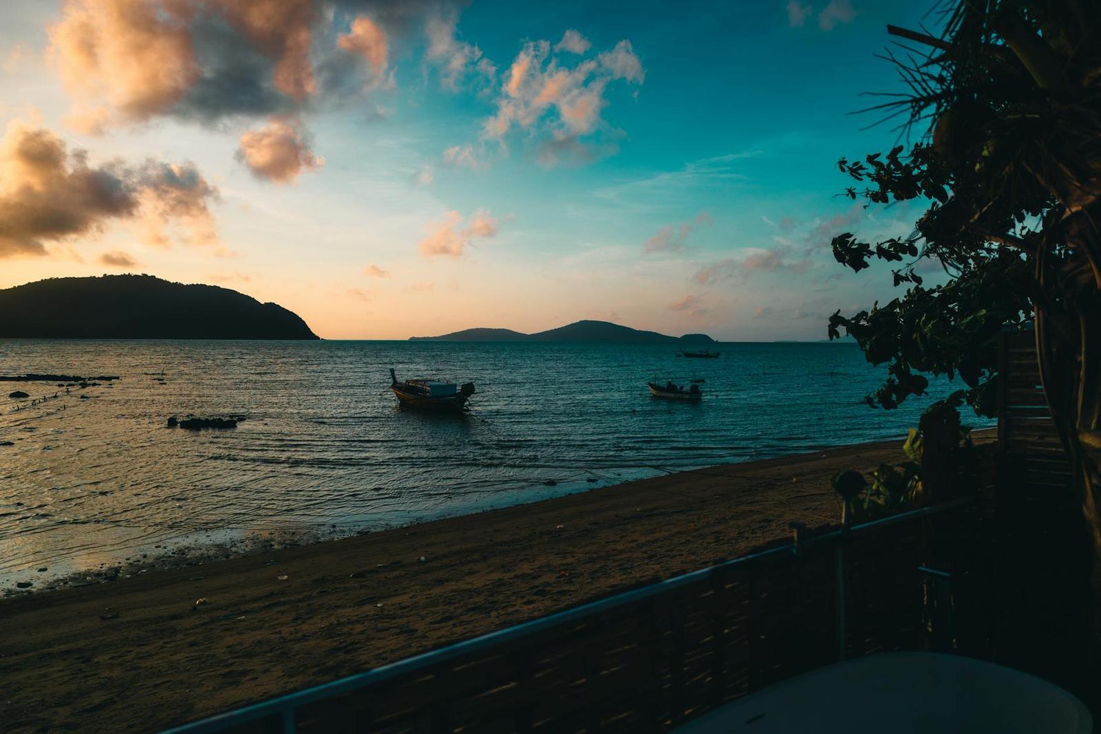 Longtail boats anchored off a beach beneath a golden sunset sky
