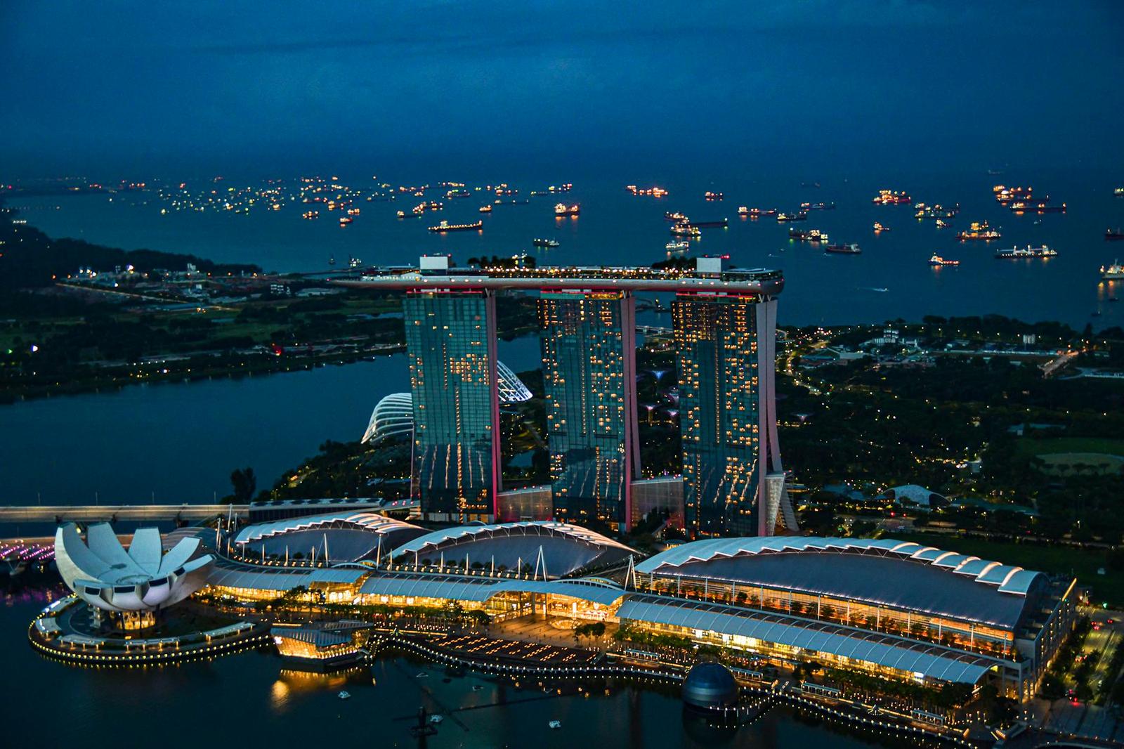 Aerial view of a lit hotel and convention centre on the bay at dusk with ships offshore