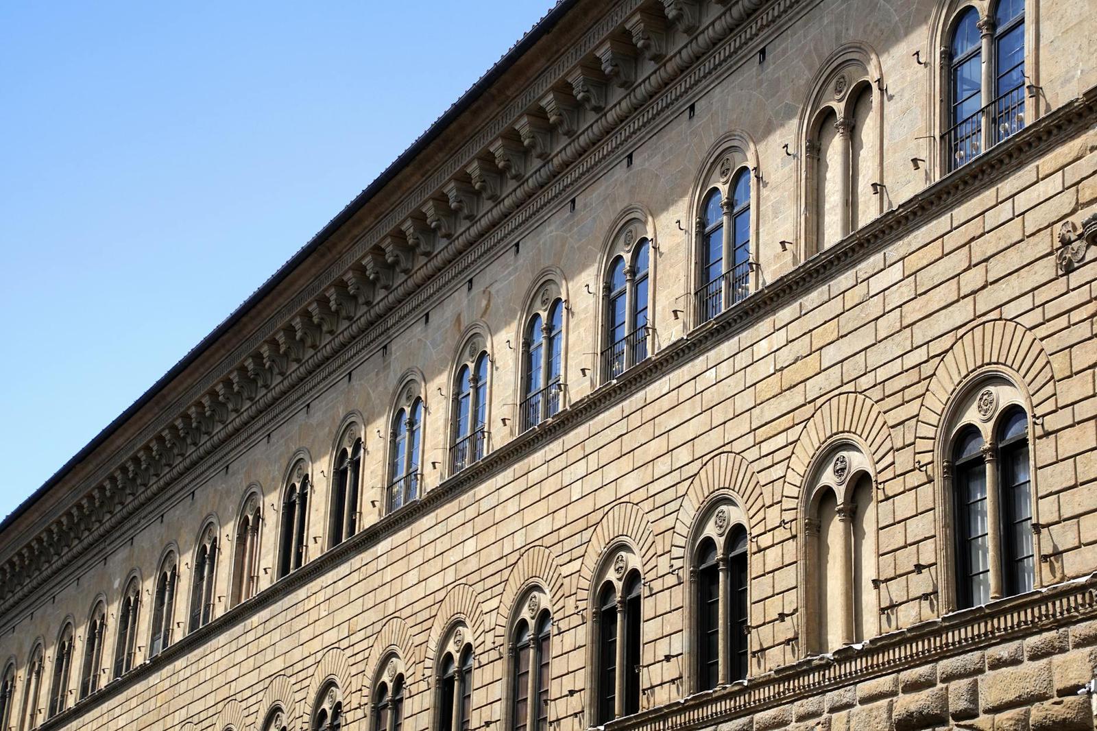 Rusticated stone palazzo facade with rows of arched windows under a clear sky