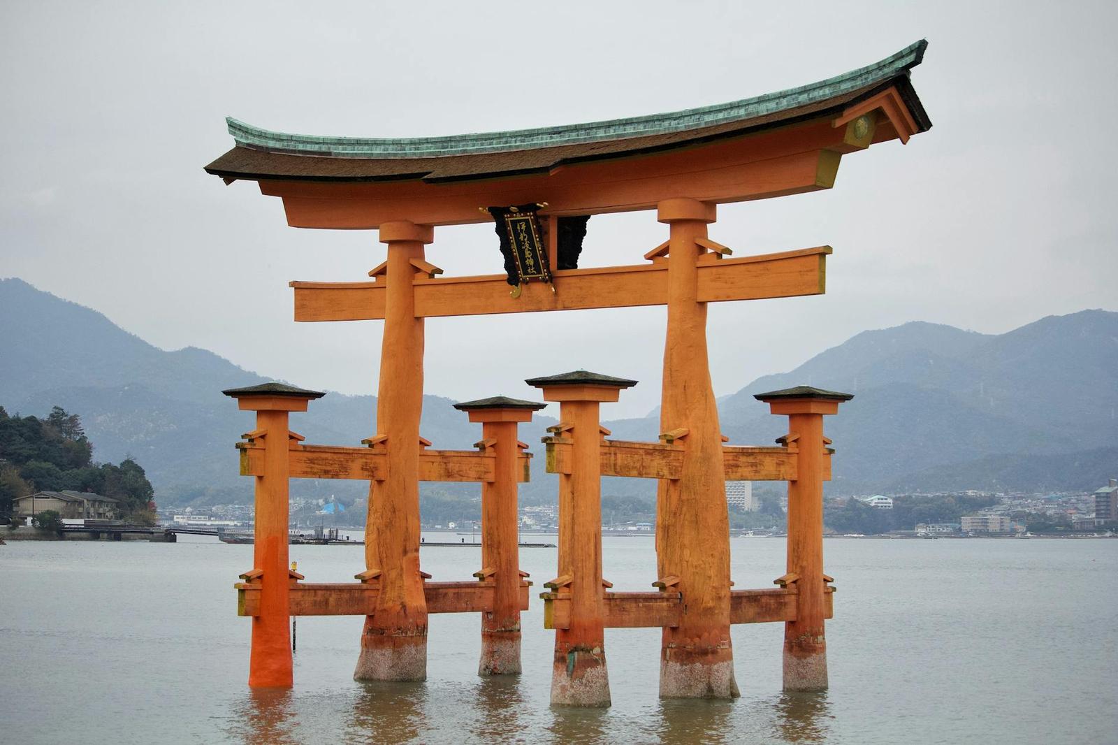Vermilion torii gate standing in shallow water against distant hills