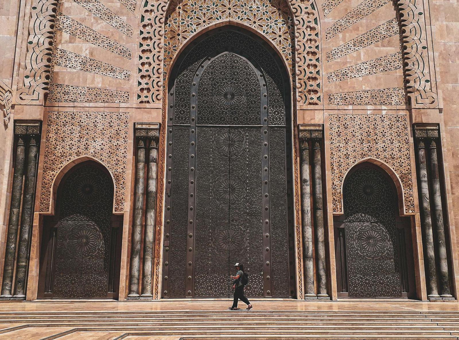 A person walking past a towering carved stone facade with ornate arched doors