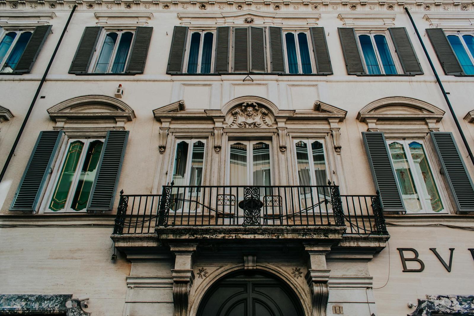 A cream-coloured palazzo facade with dark shutters and a wrought-iron balcony