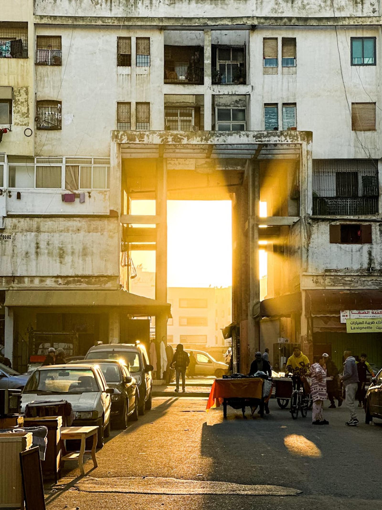 Golden sunlight streaming through an archway onto a street market at dusk