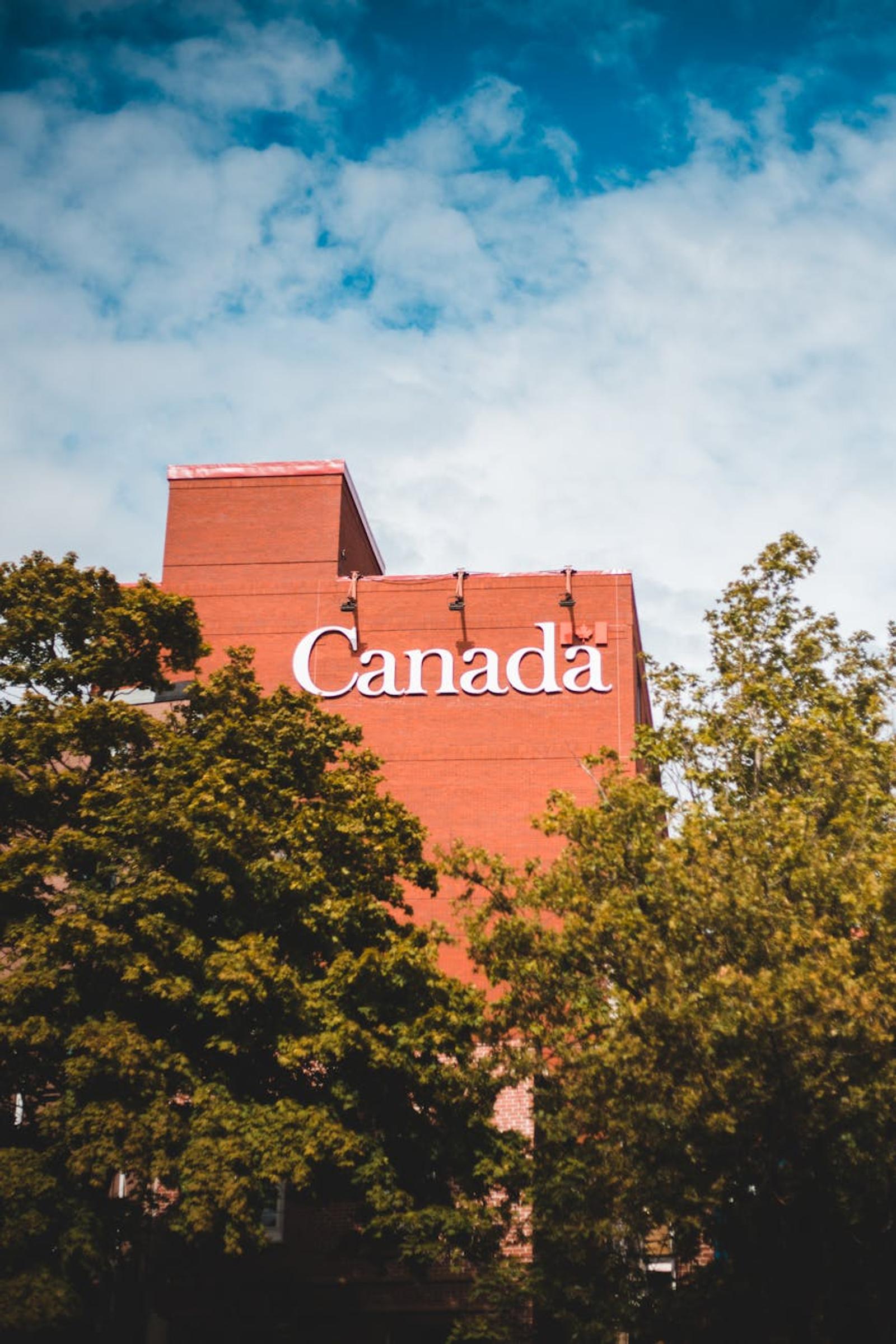 Modern brick building featuring 'Canada' signage surrounded by lush trees and blue sky