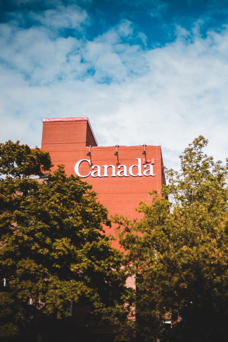Modern brick building featuring 'Canada' signage surrounded by lush trees and blue sky