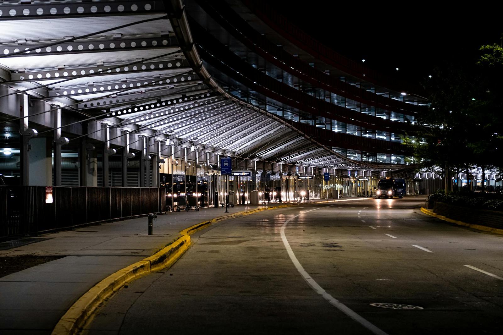An empty airport terminal drop-off curb lit beneath a covered canopy at night