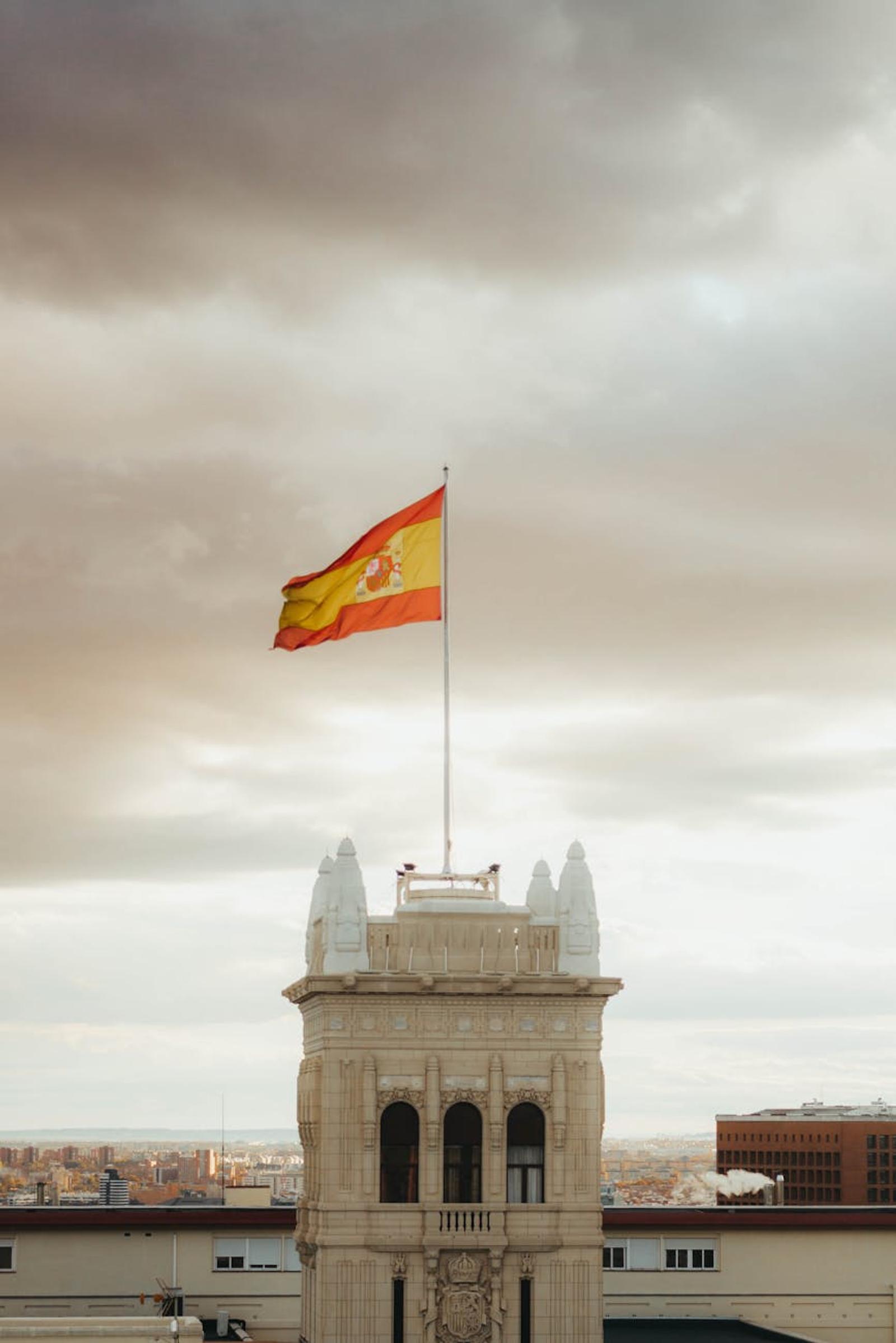 The Spanish flag waves atop an iconic building in Madrid against a dramatic sky