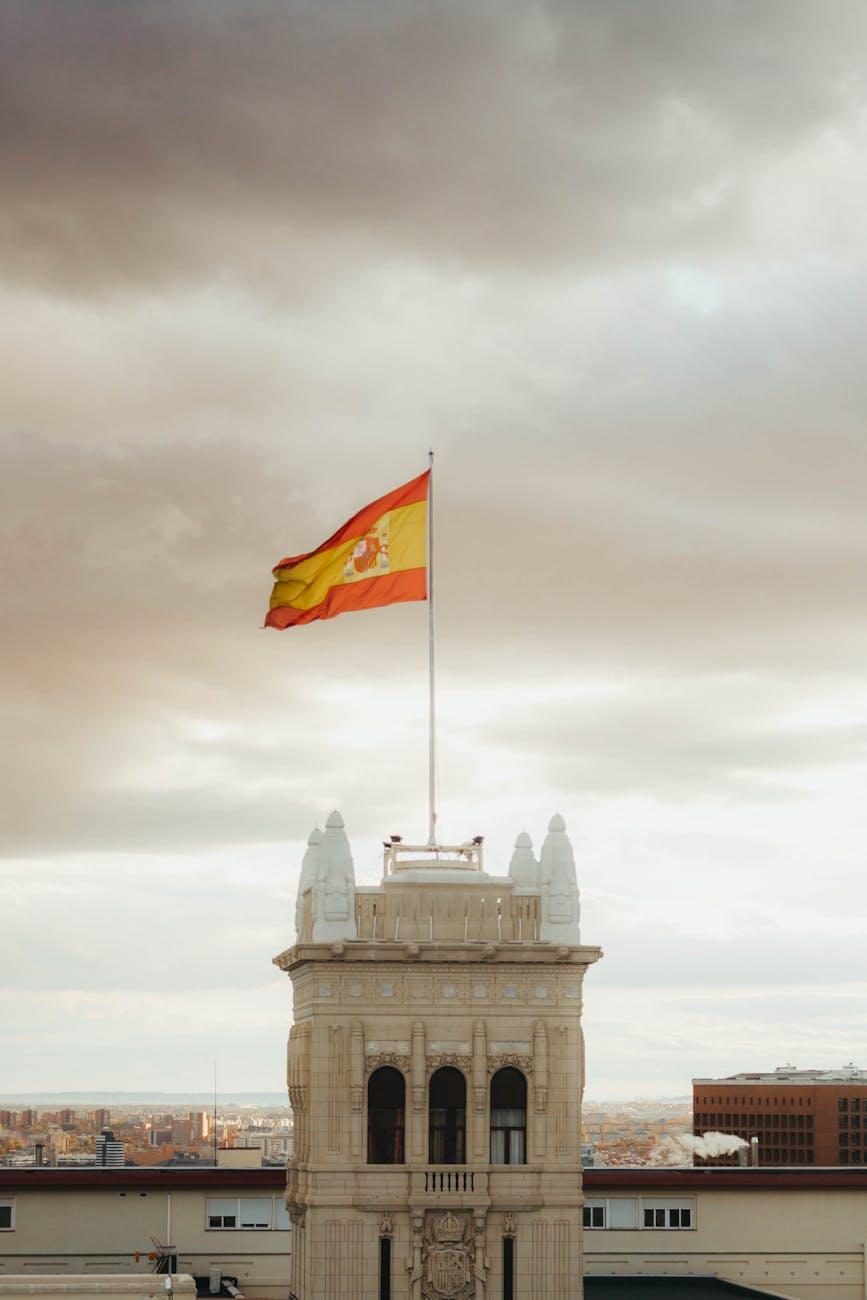 The Spanish flag waves atop an iconic building in Madrid against a dramatic sky
