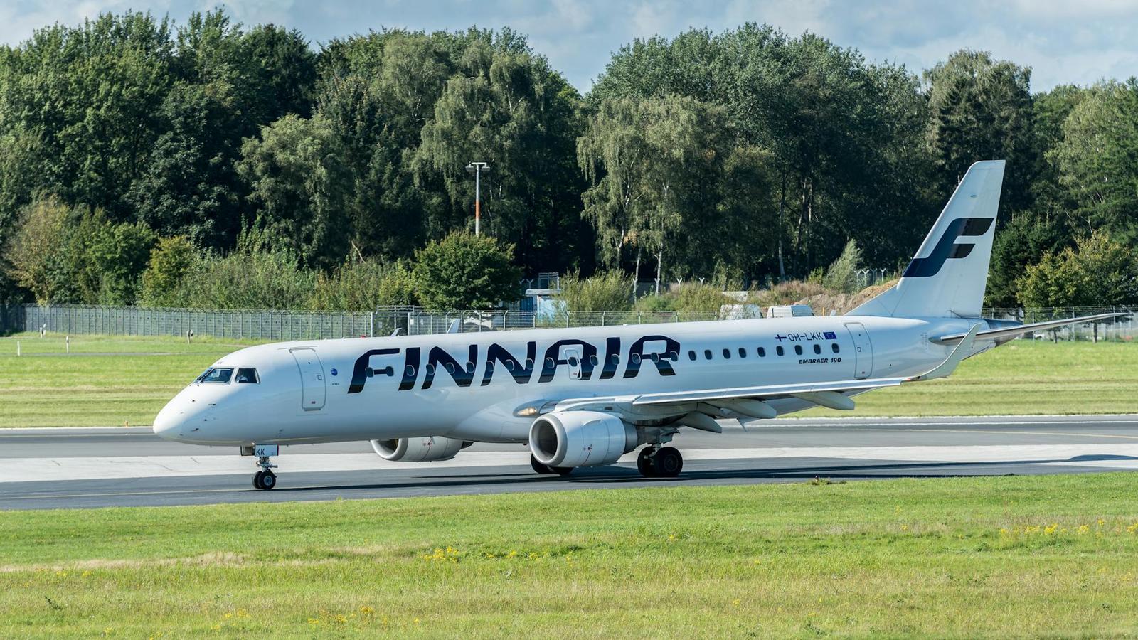 A Finnair jet taxiing on a runway past a tree line