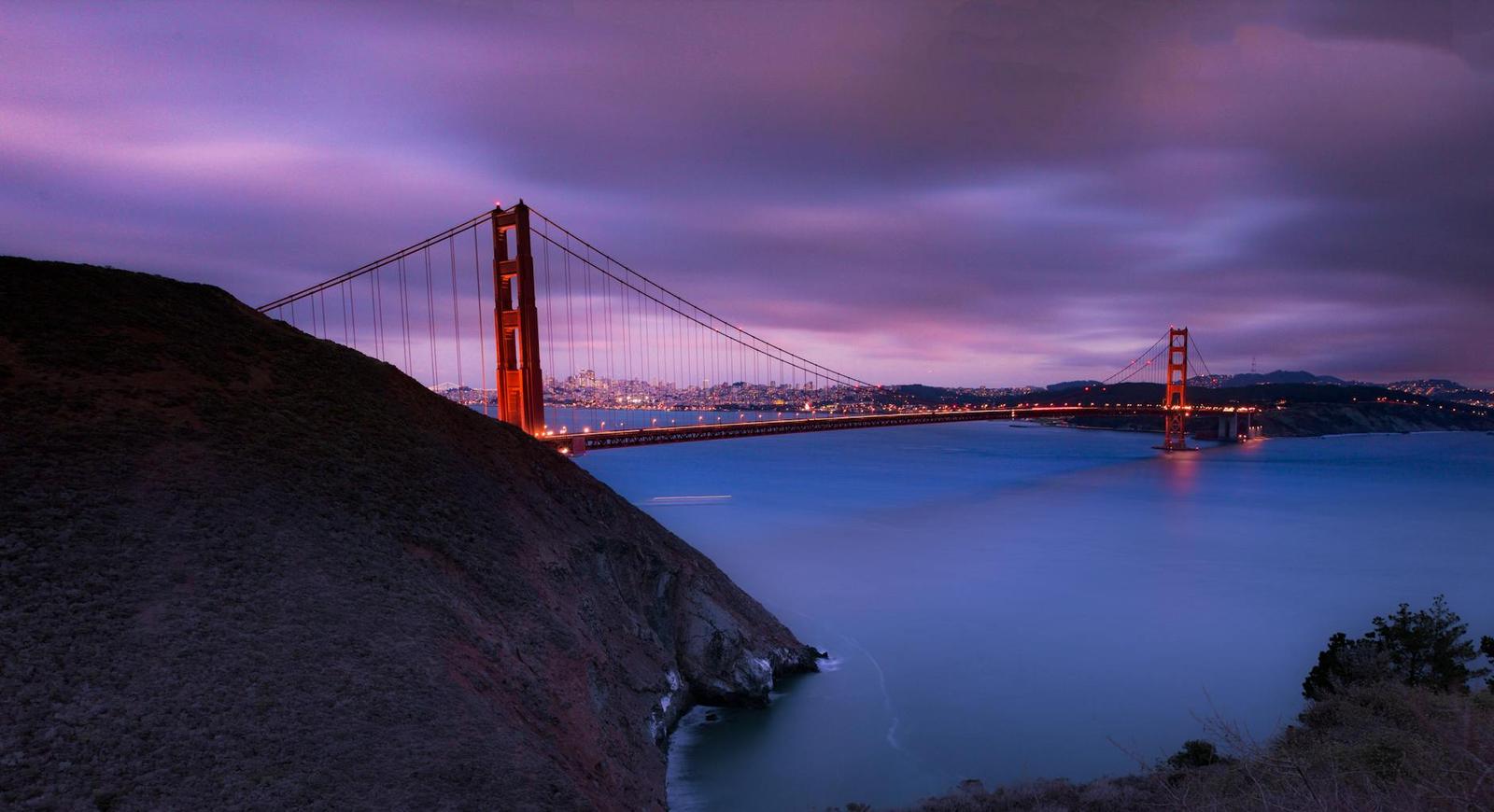 A suspension bridge spanning a bay at dusk under pink clouds
