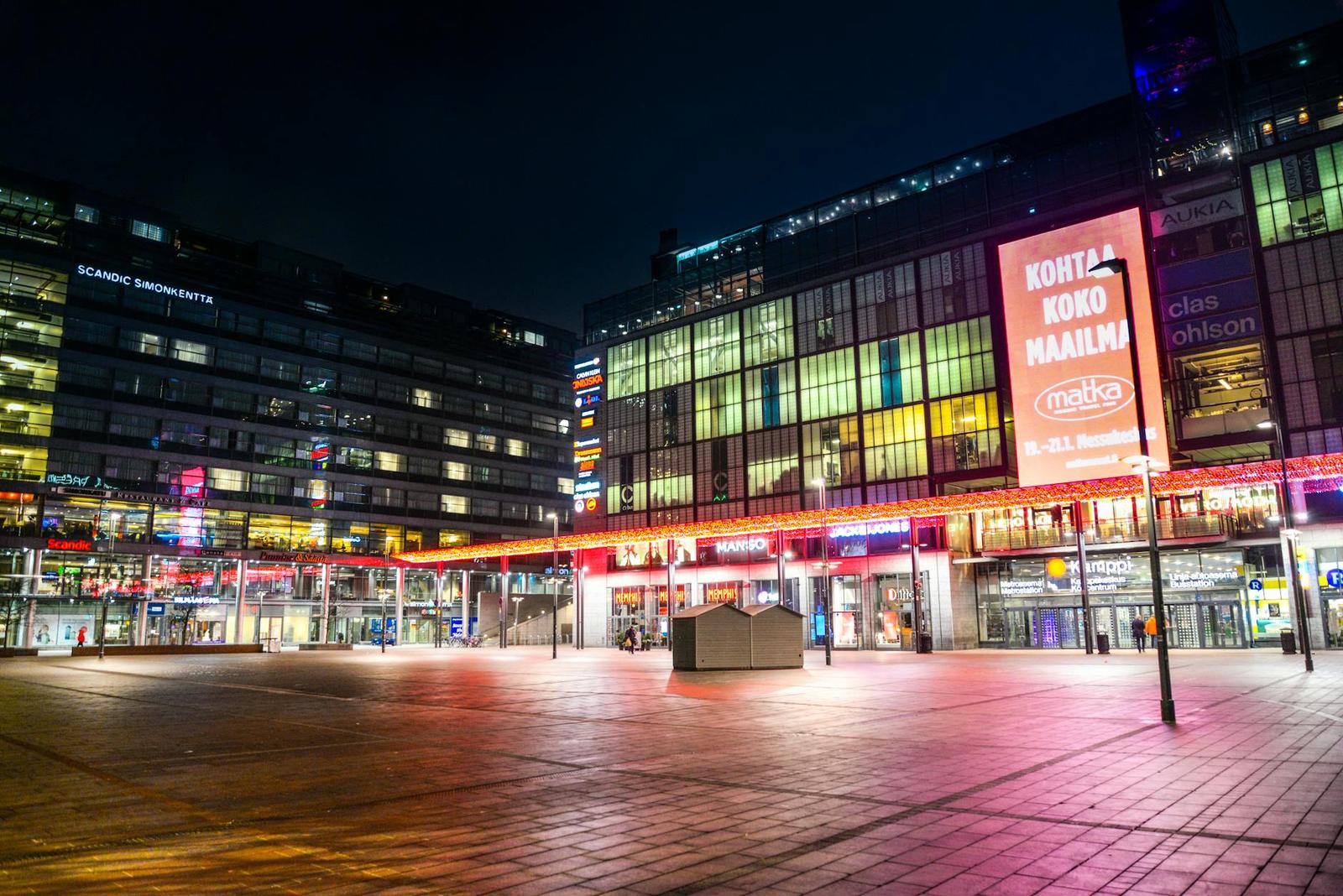 An illuminated city plaza with neon signs at night