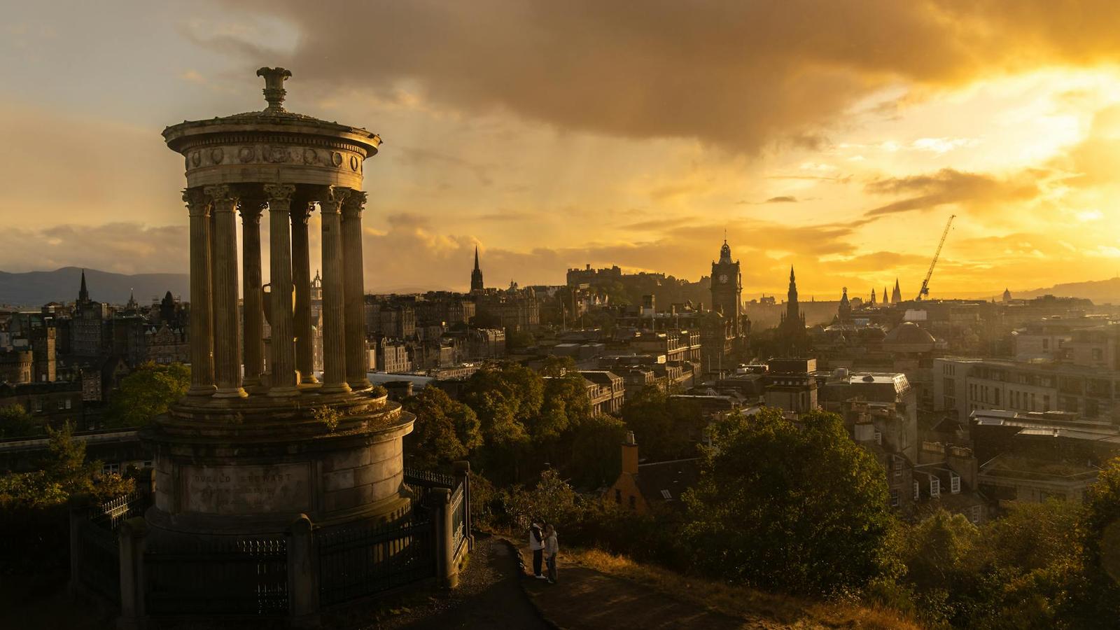 A classical column monument overlooking a golden-lit city skyline at sunset