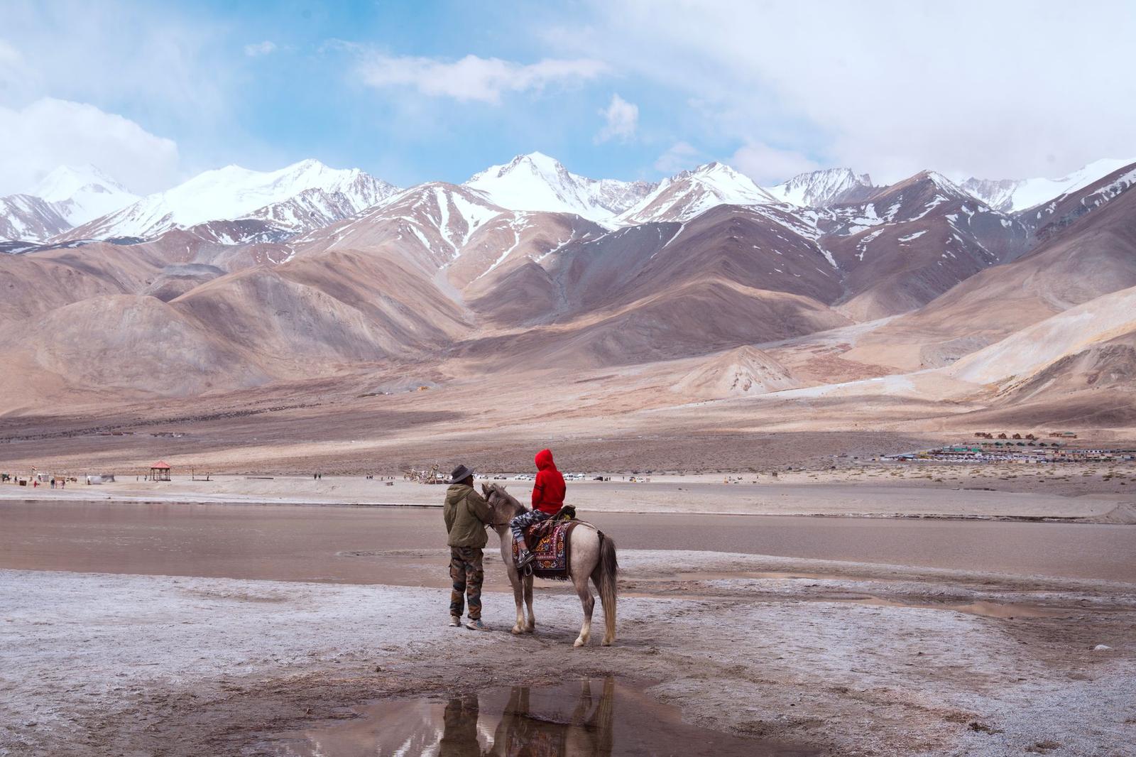 Figures with a horse standing on a dry lakebed before snow-capped peaks