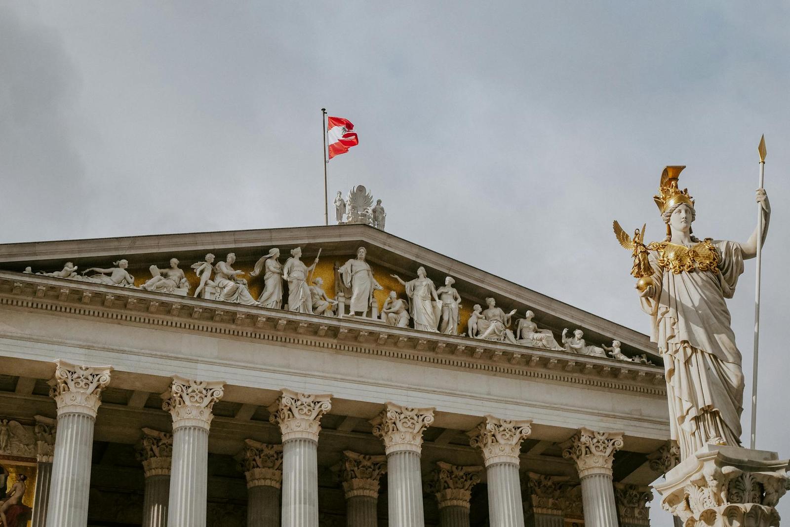 A gilded statue beside a classical pediment with carved figures and a flag