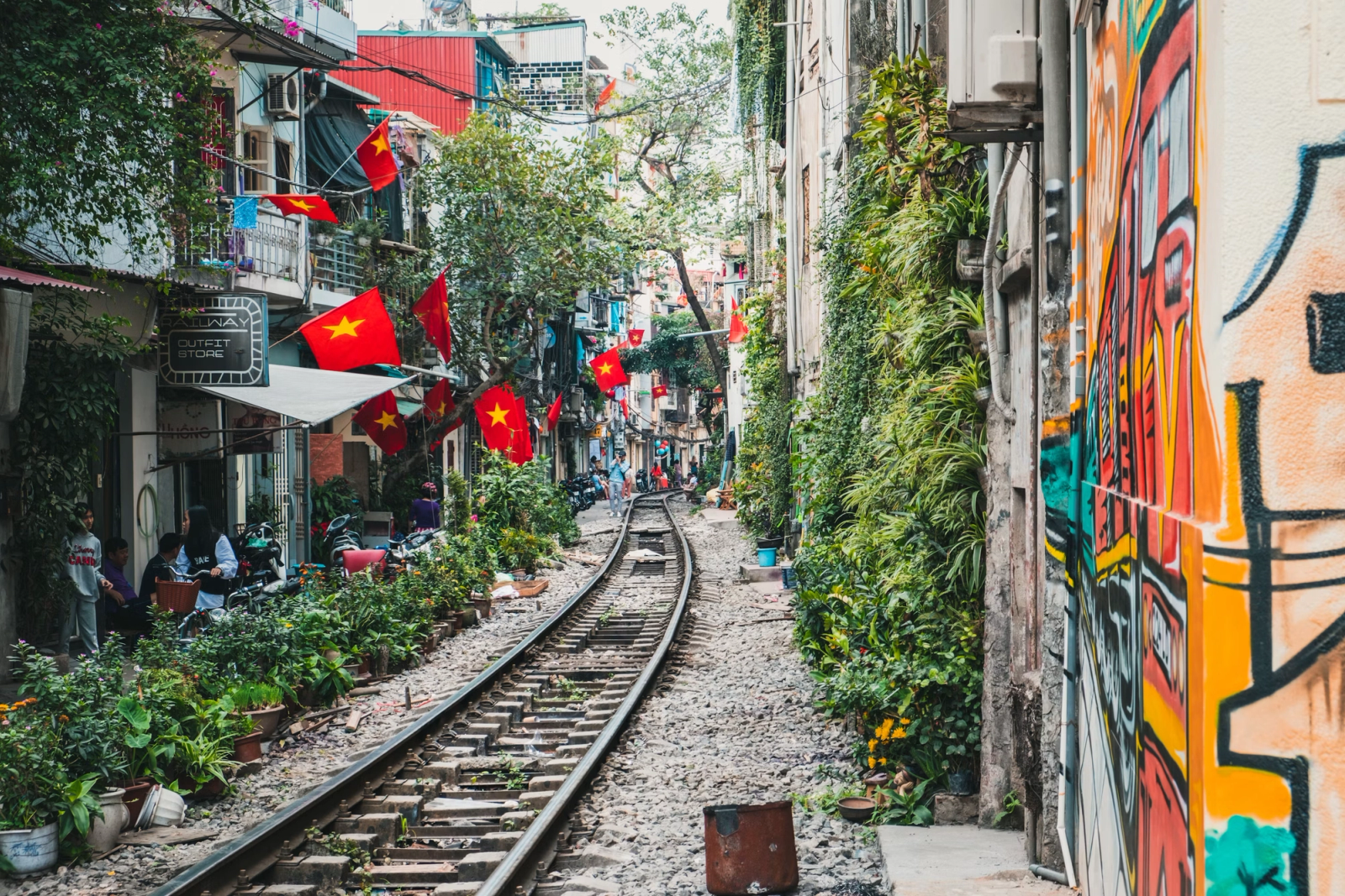 A narrow street with train tracks running past flag-draped balconies and murals