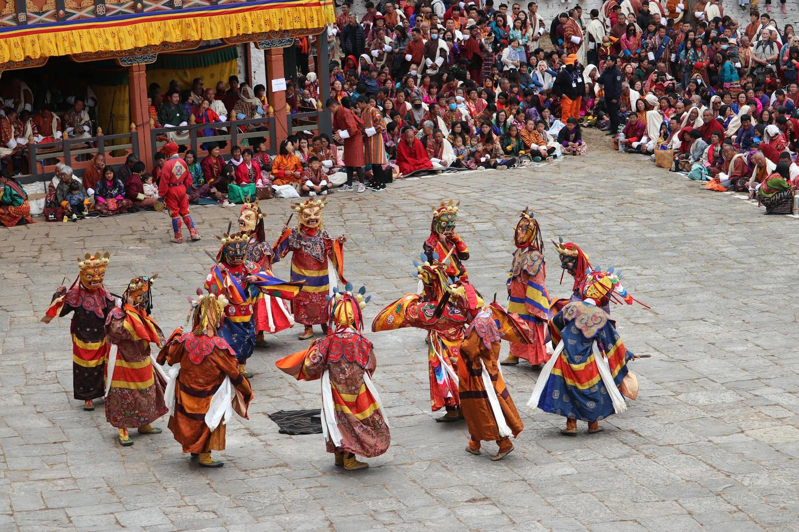Masked festival dancers in colourful costume performing before a seated crowd
