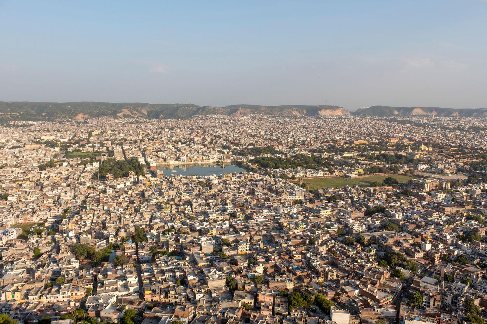 A dense sprawling city seen from above with a small lake in the distance