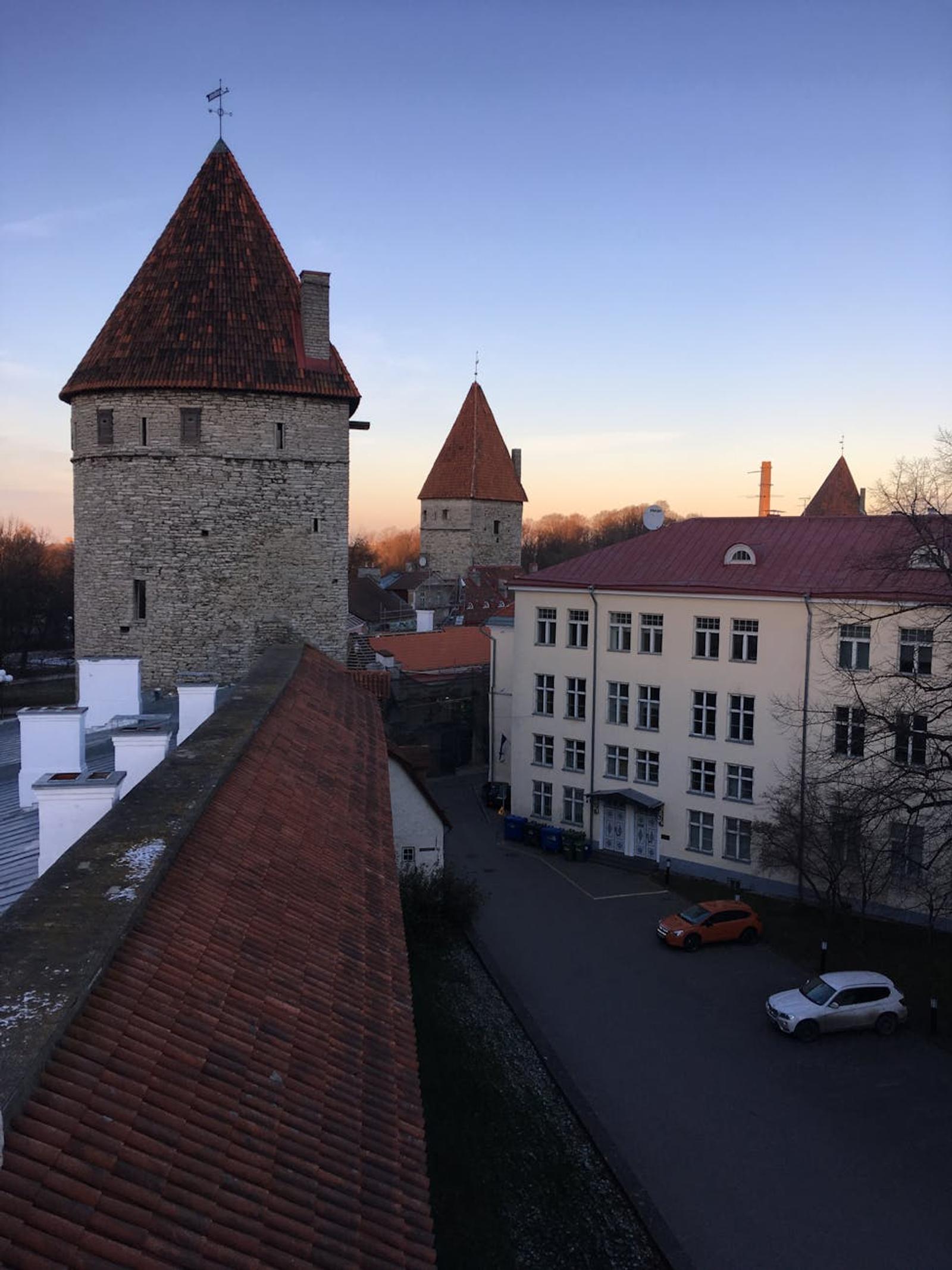 Medieval stone towers with conical red roofs overlooking a quiet street at dusk
