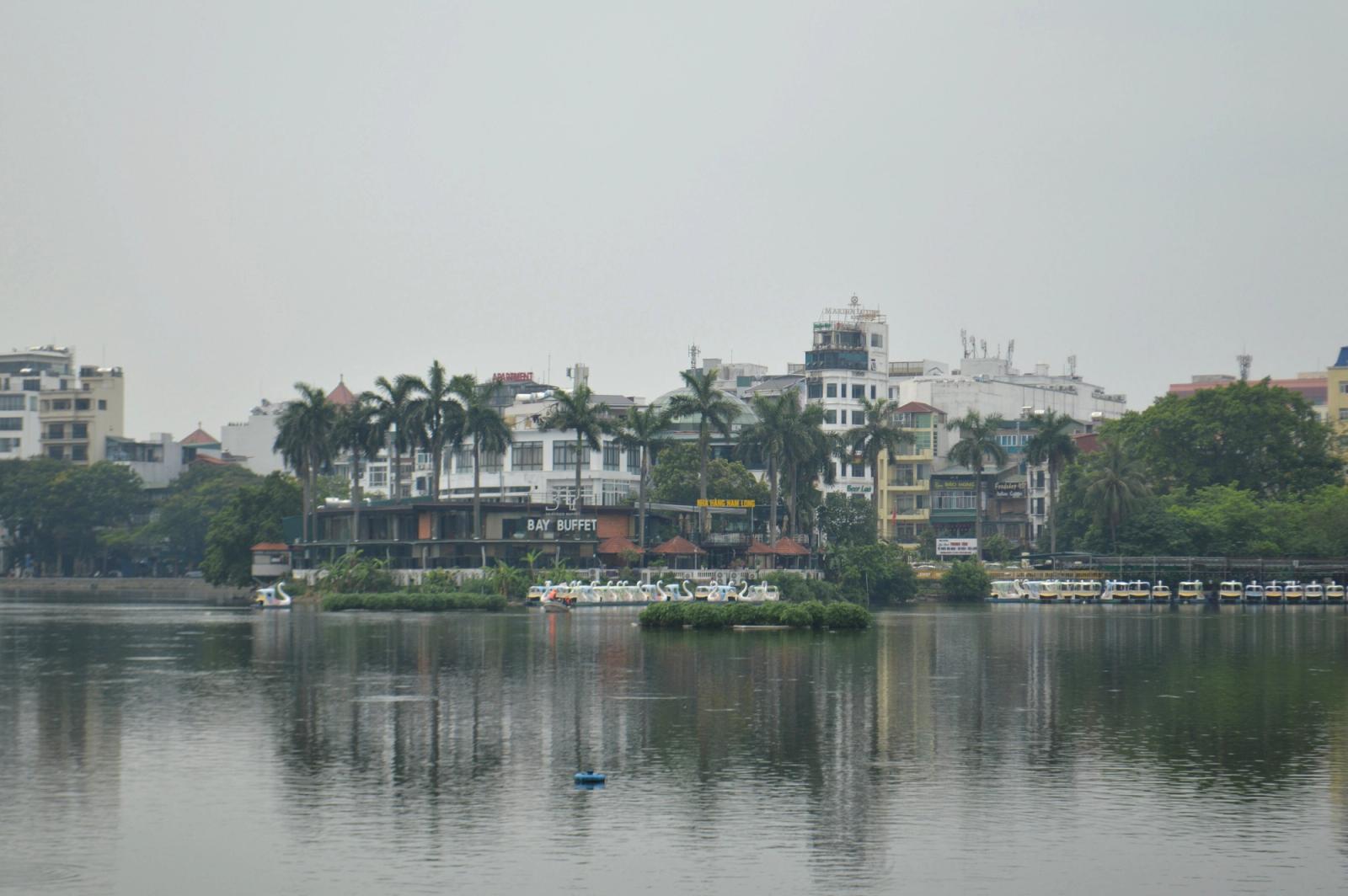 Serene view of Truc Bach Lake in Hanoi, showcasing buildings, palm trees, and boats