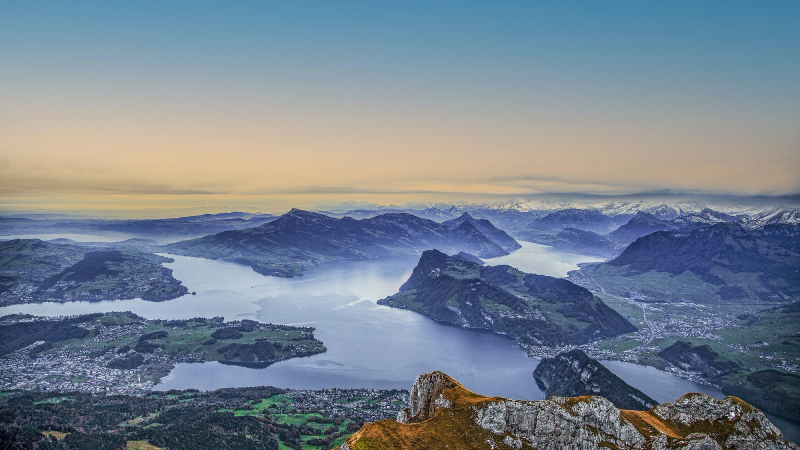 Aerial view of a mountain lake and forested peaks at dusk from a summit