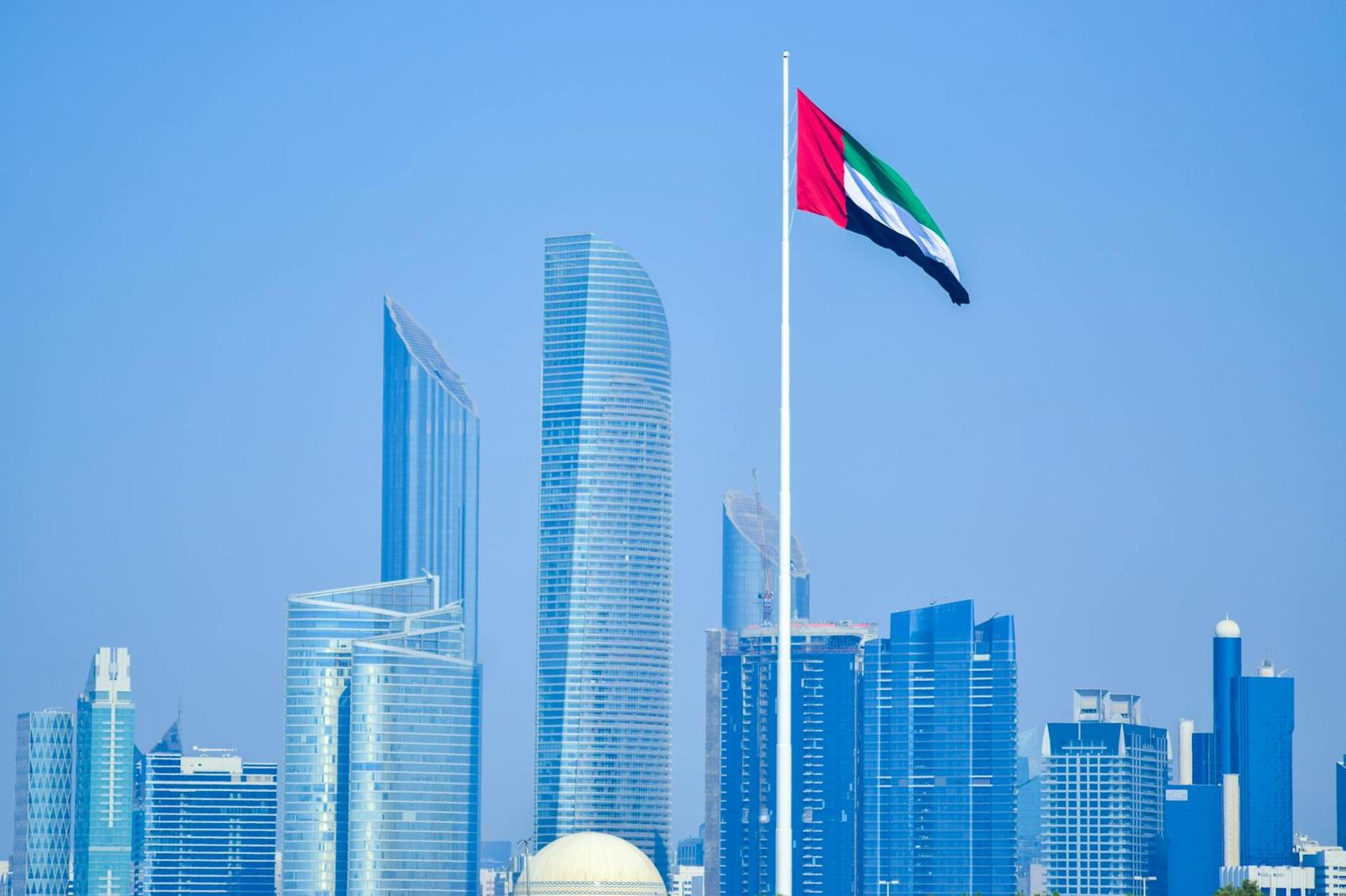 A national flag on a tall pole rising above a glass tower skyline
