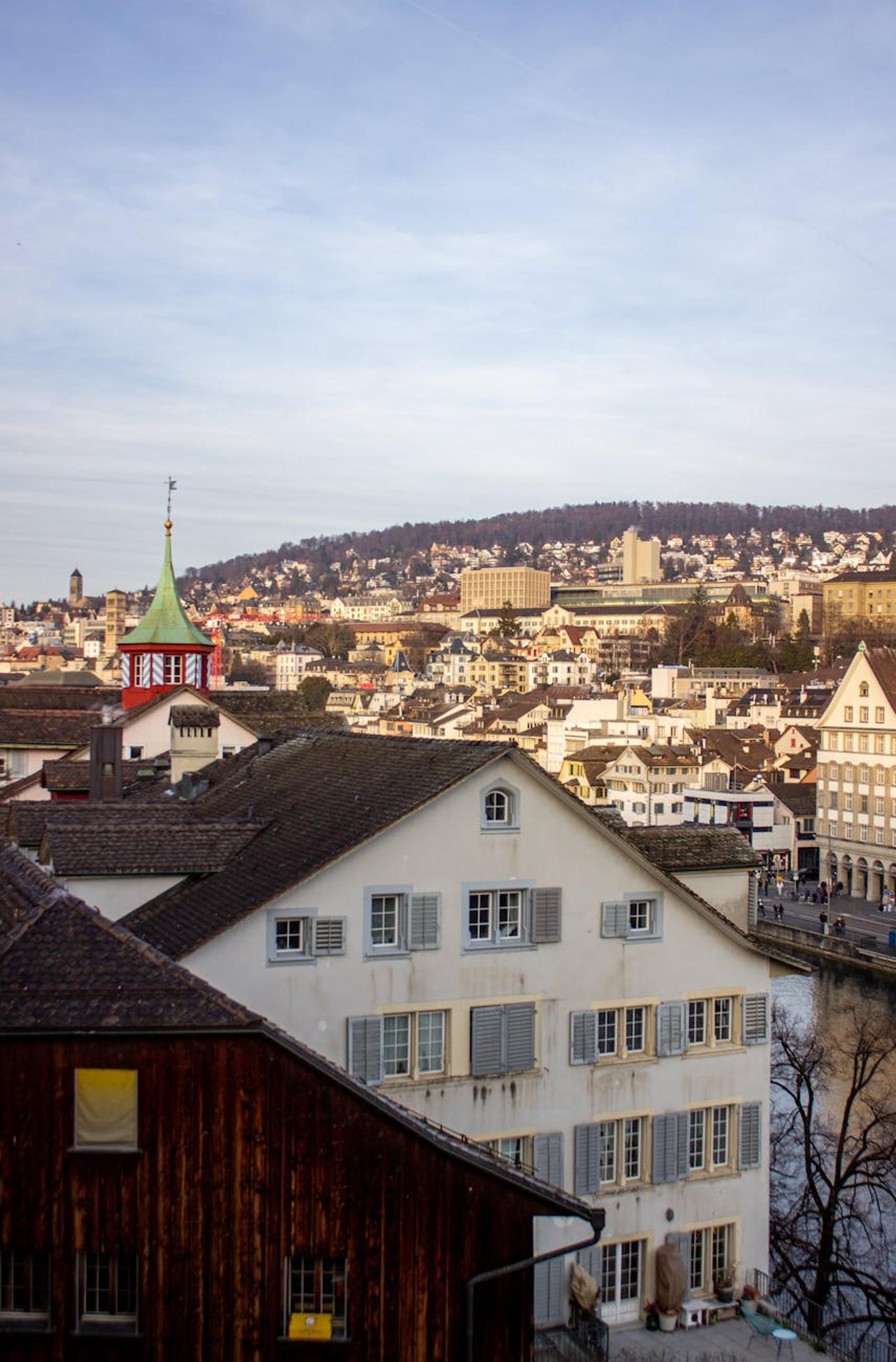 Green copper spire and rooftops overlooking a hillside city and river