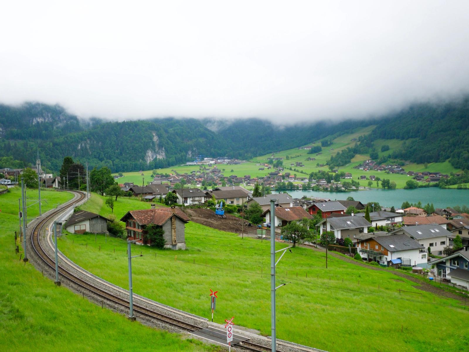 Railway curving through a misty green valley past a lakeside village