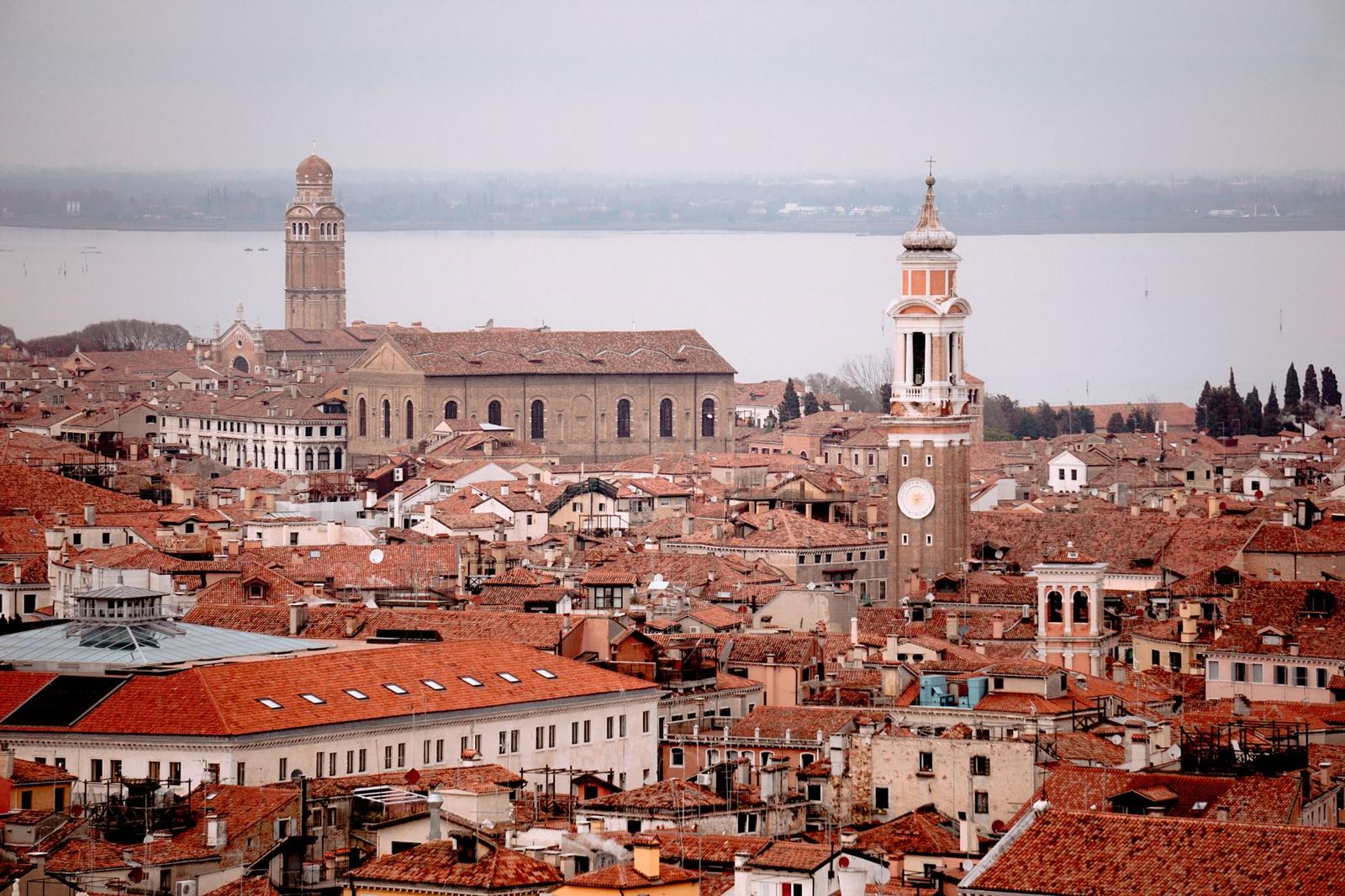 Terracotta rooftops and a bell tower overlooking a lagoon under hazy sky