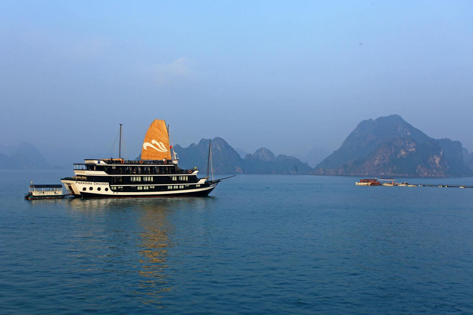 Traditional wooden cruise boat with an orange sail among limestone islands