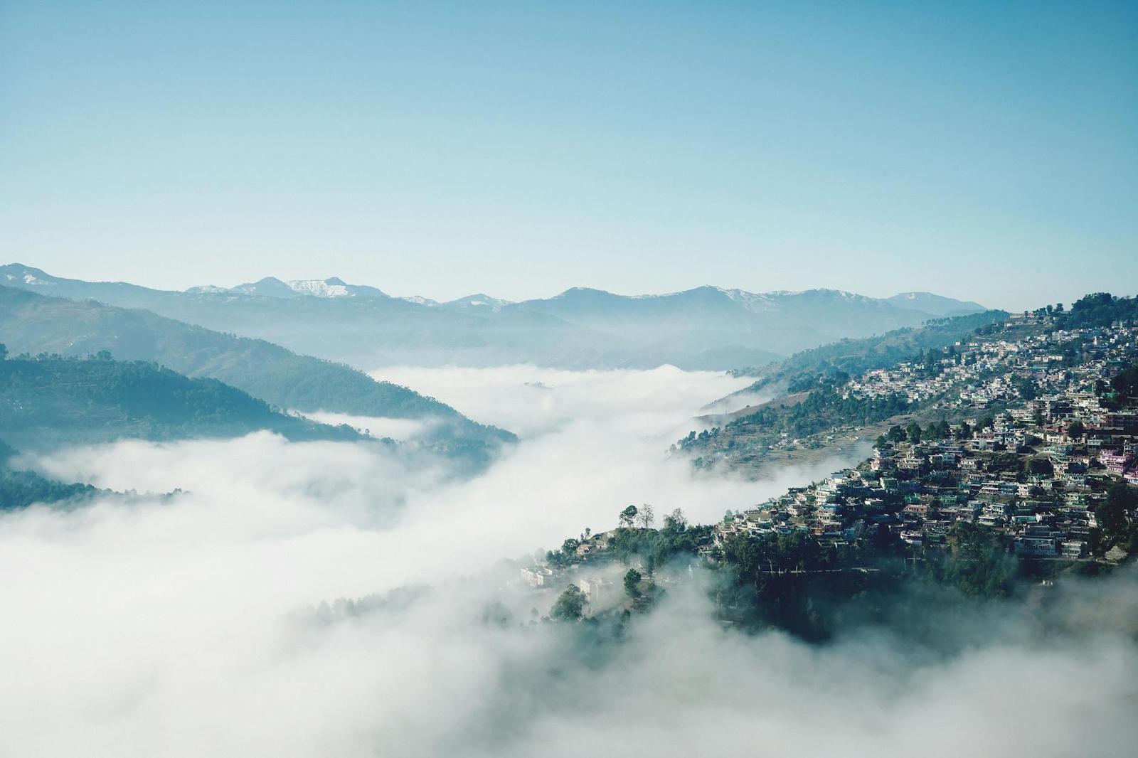 A hillside town emerging from a sea of fog beneath distant snow-dusted peaks