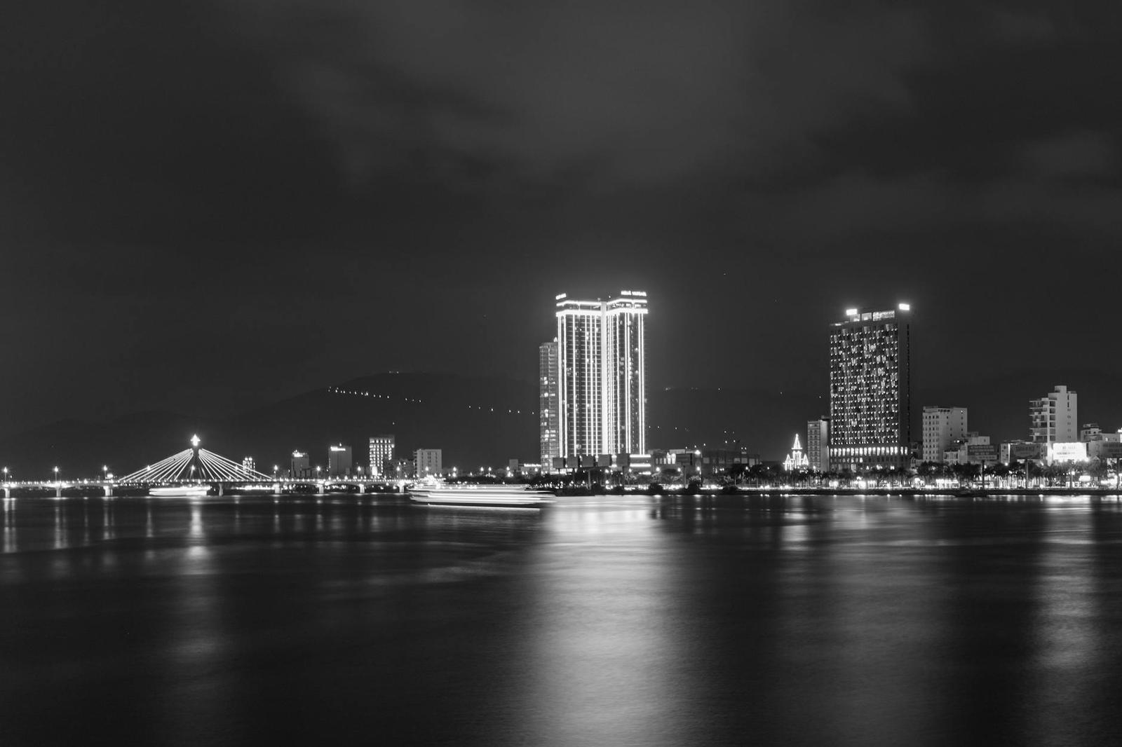Illuminated high-rise towers and a lit bridge reflected in a river at night