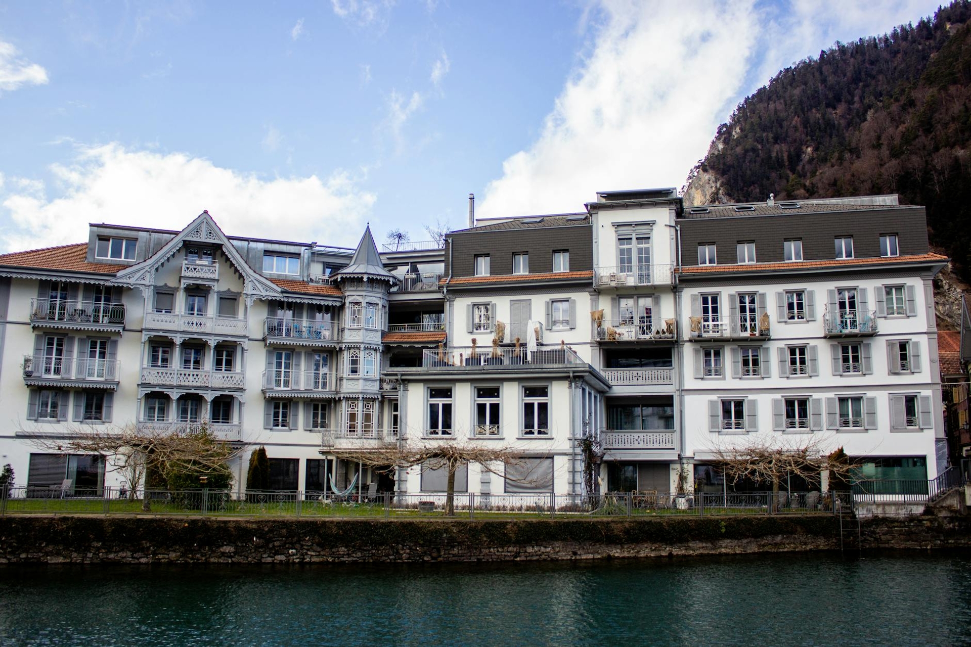 A row of alpine hotel buildings with turrets and balconies along a riverbank