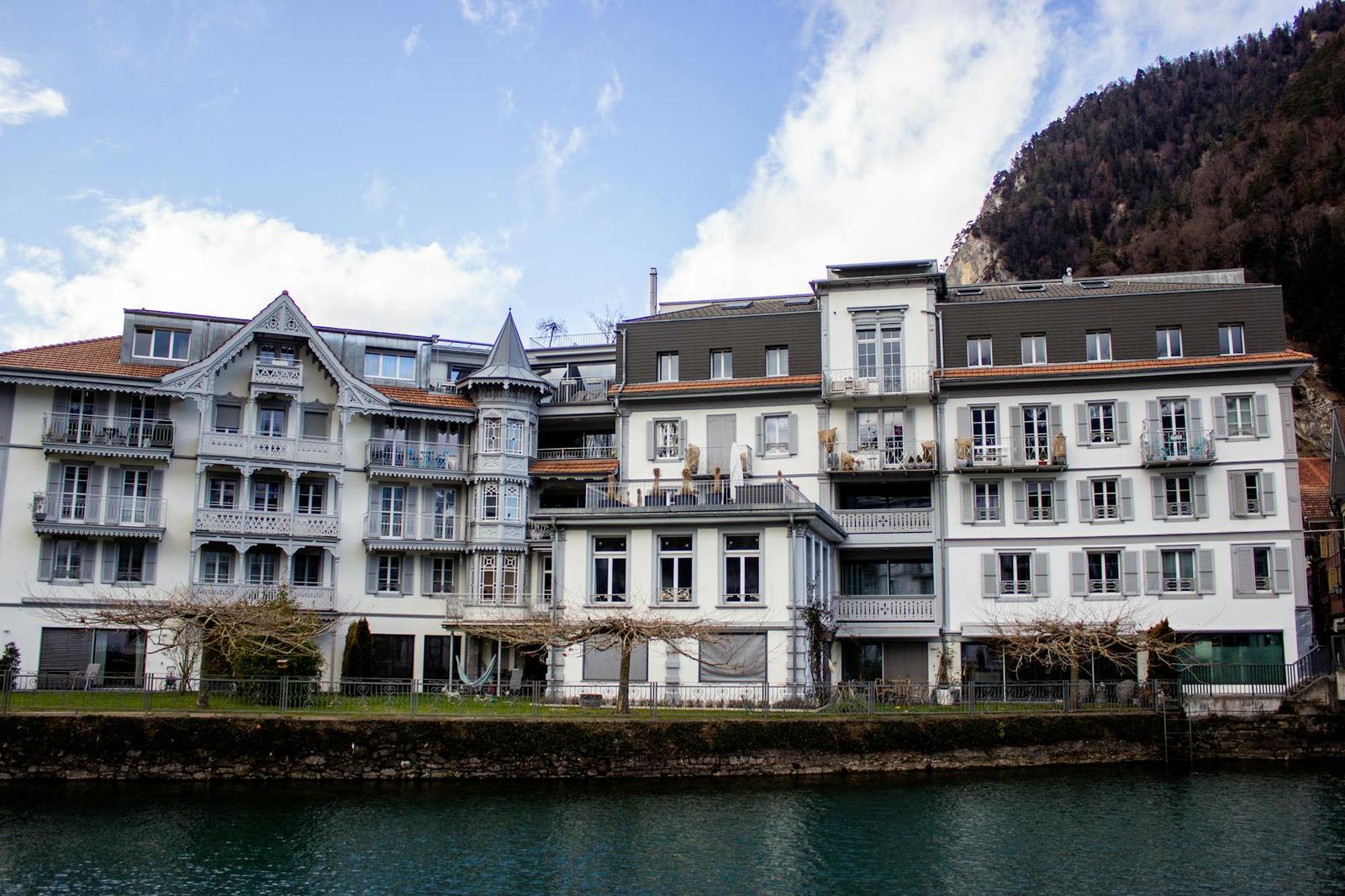 A row of alpine hotel buildings with turrets and balconies along a riverbank