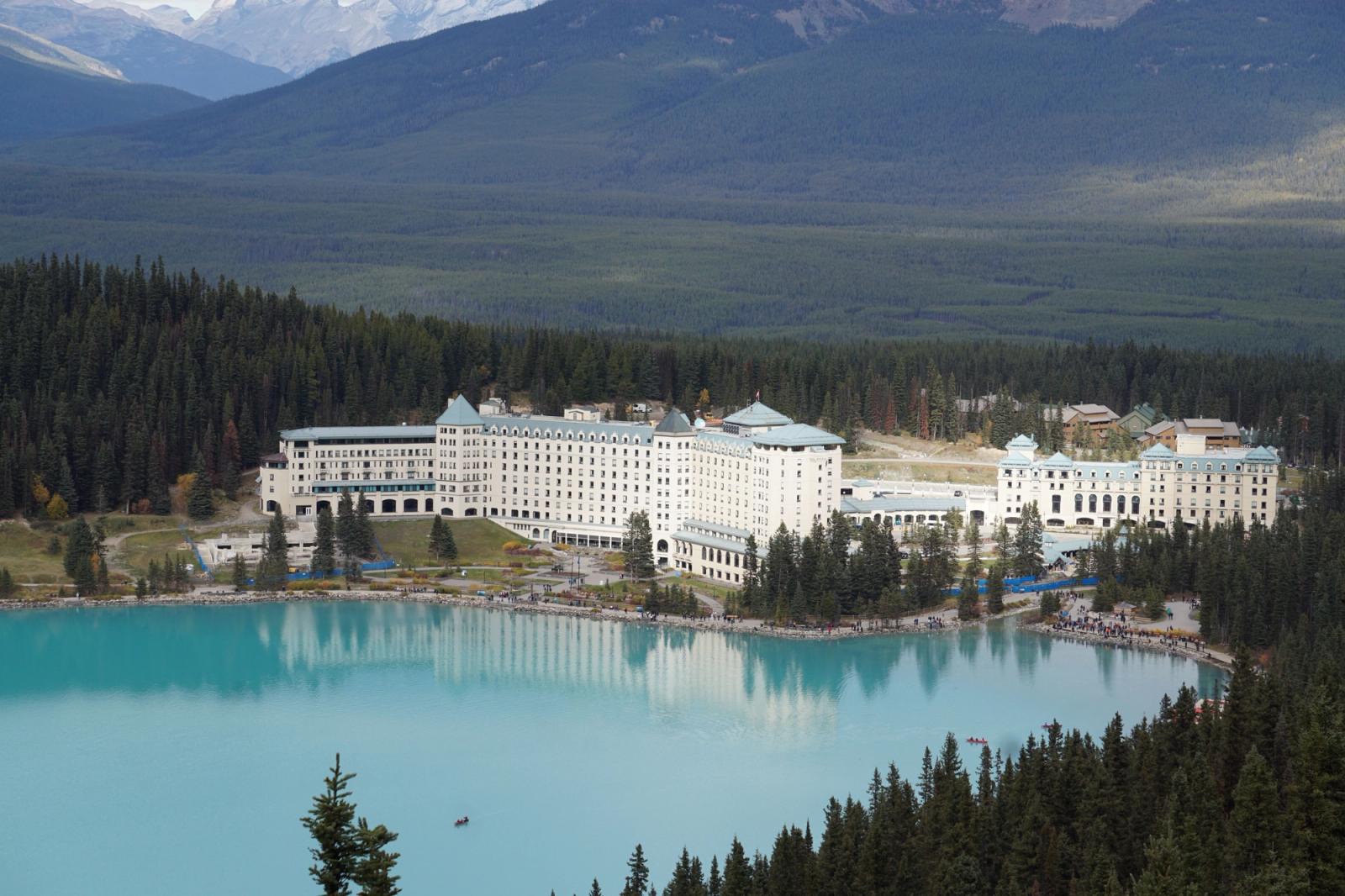 A stunning aerial view of Fairmont Chateau Lake Louise with turquoise waters and forested mountains in Canada