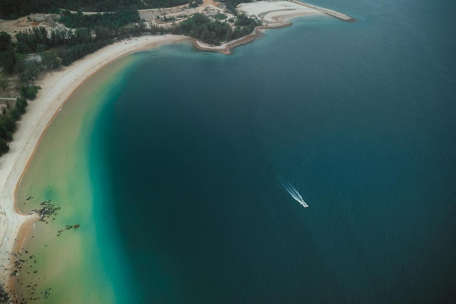 Aerial view of a boat leaving a wake across a sheltered turquoise bay