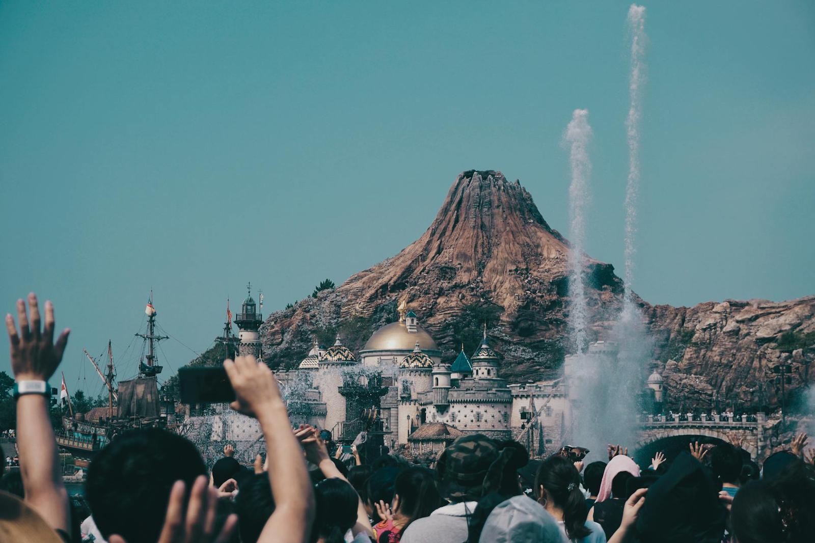 A crowd raising their arms as water jets shoot up before a volcano-shaped structure