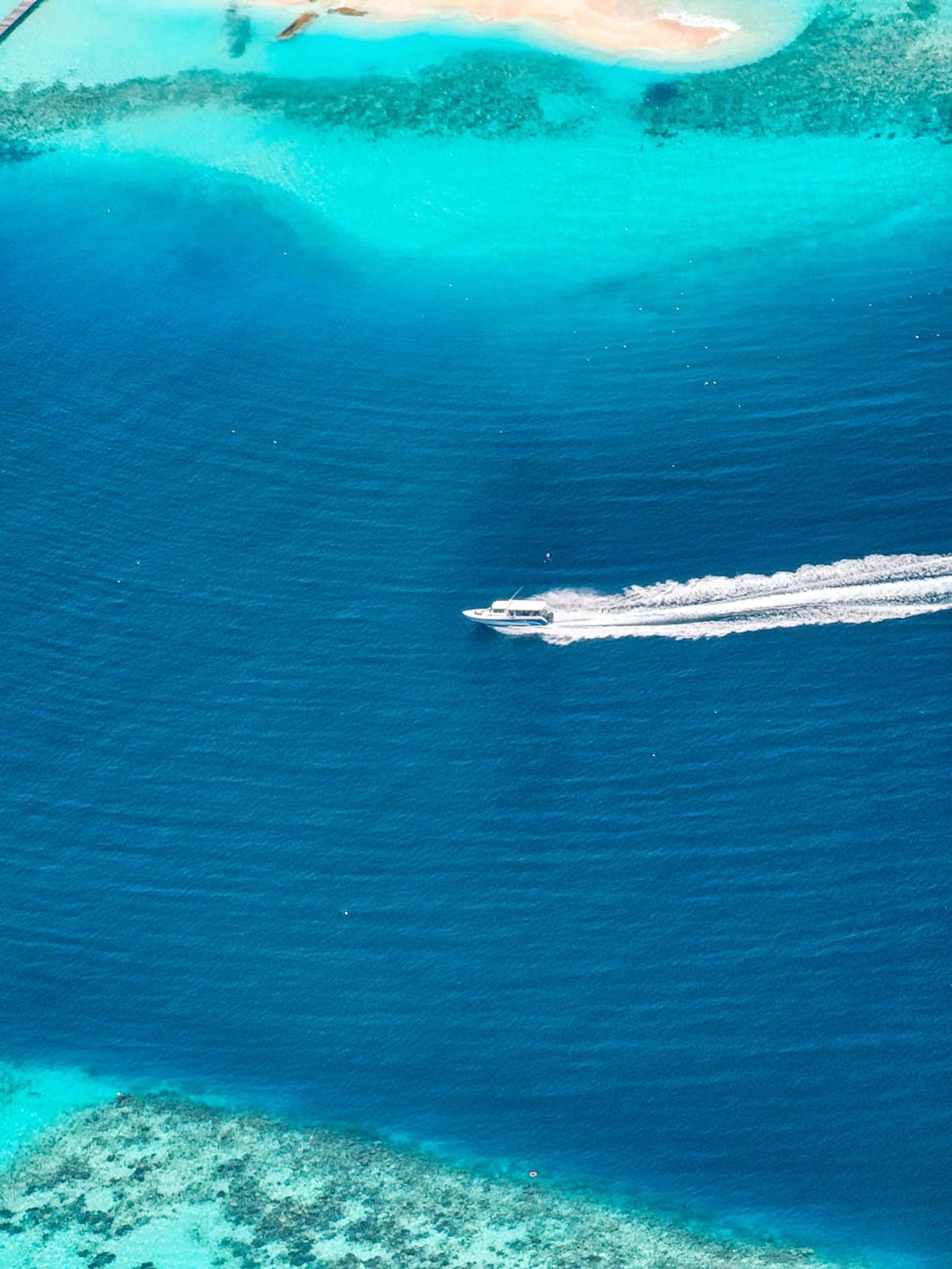 Aerial view of a boat trailing a wake between a coral reef and open sea