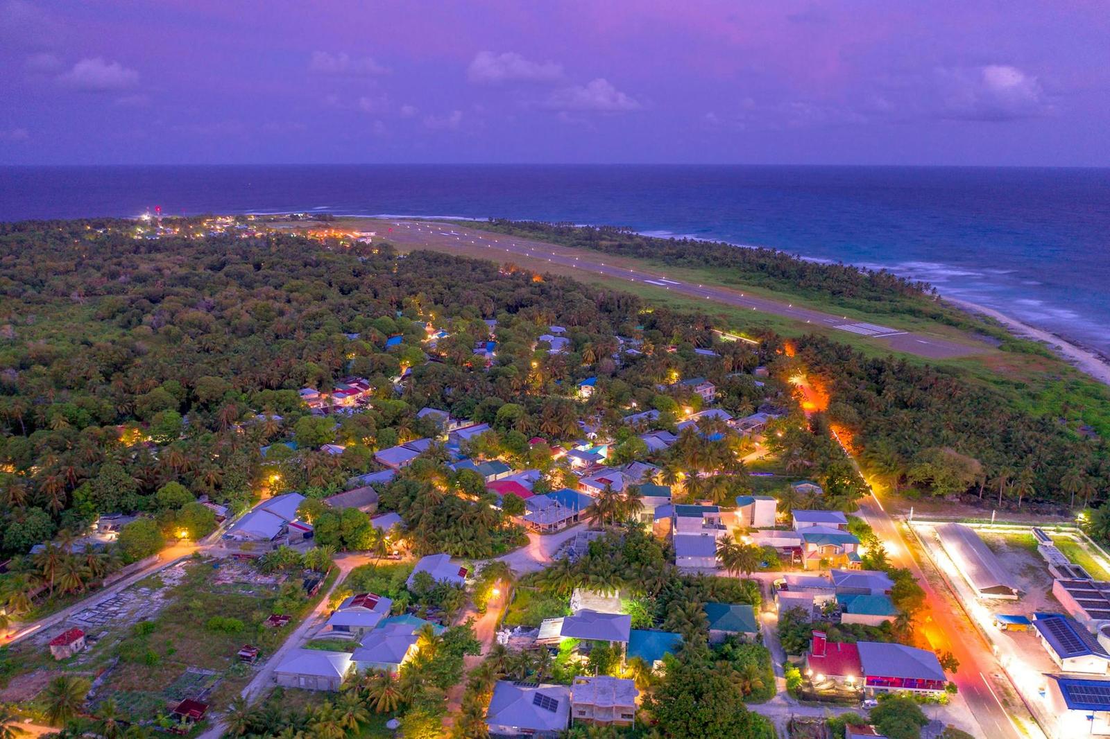 Aerial view of a village lit up at dusk beside a runway and the sea