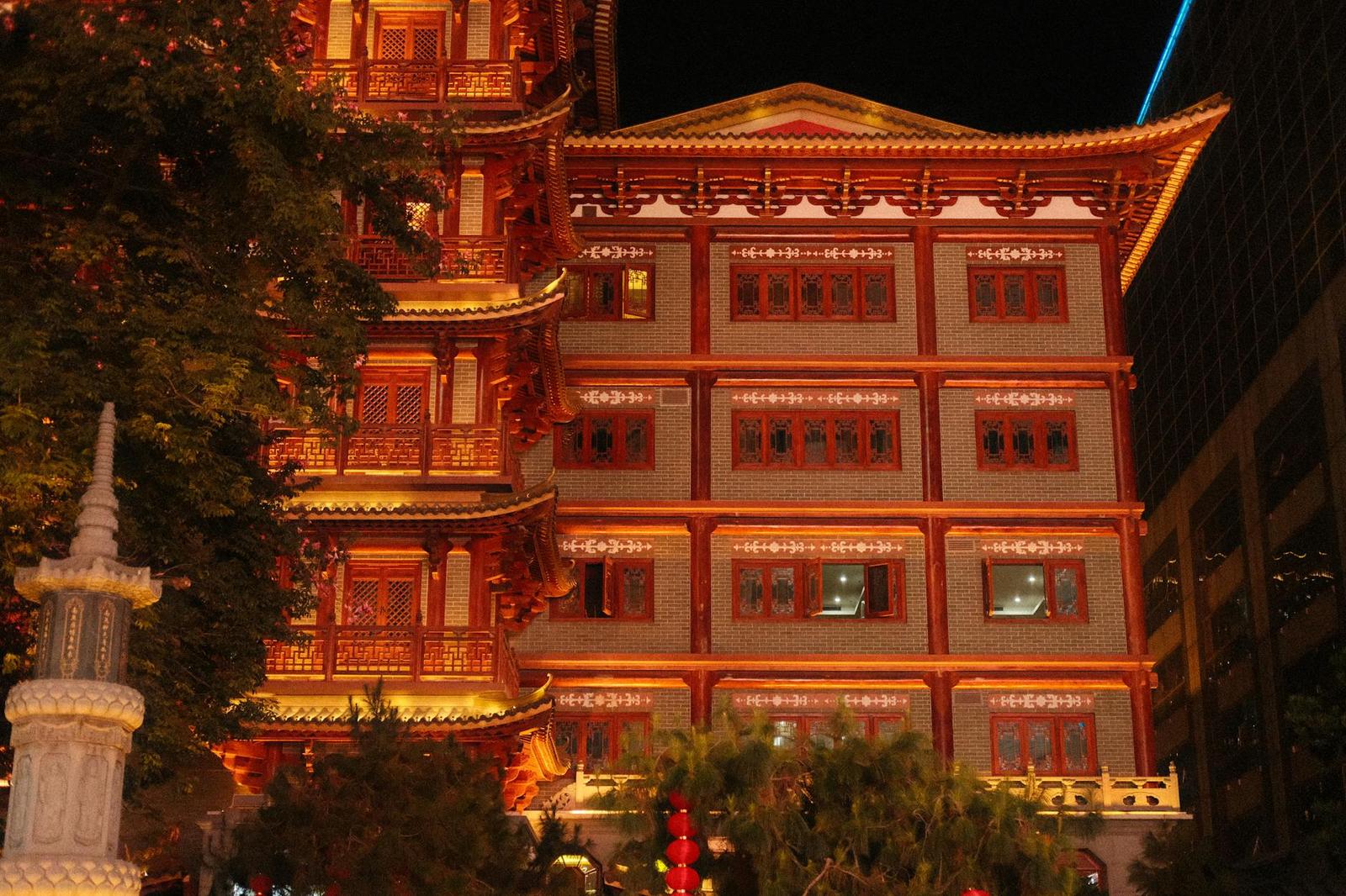 A pagoda-style building lit red and gold at night among city trees