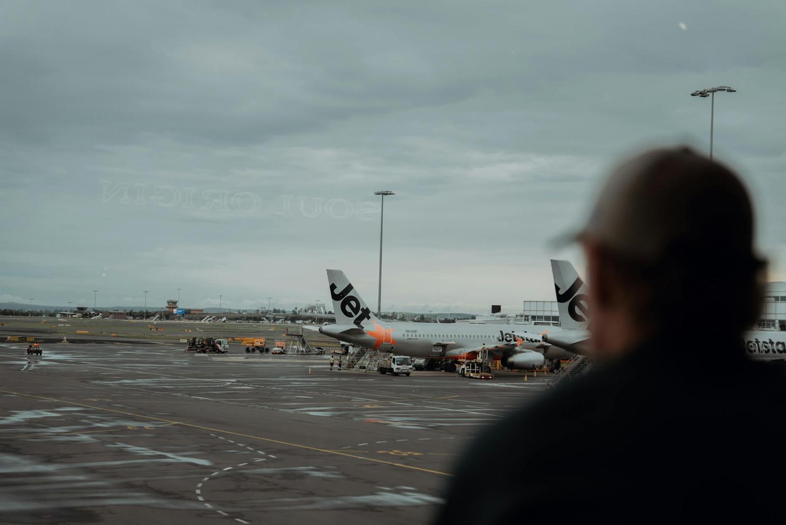 A traveller in silhouette watches planes on a rainy airport tarmac