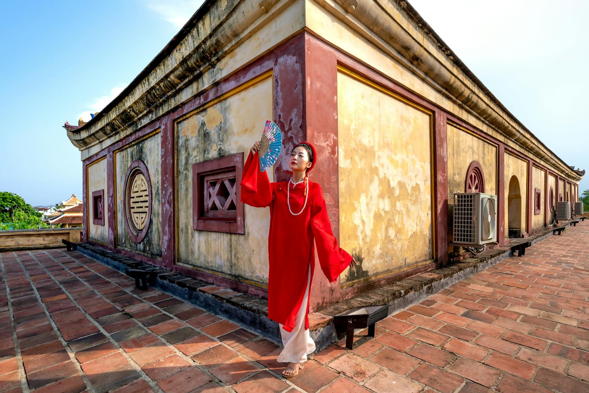 Woman in a red silk dress holding a fan beside a weathered ochre temple wall