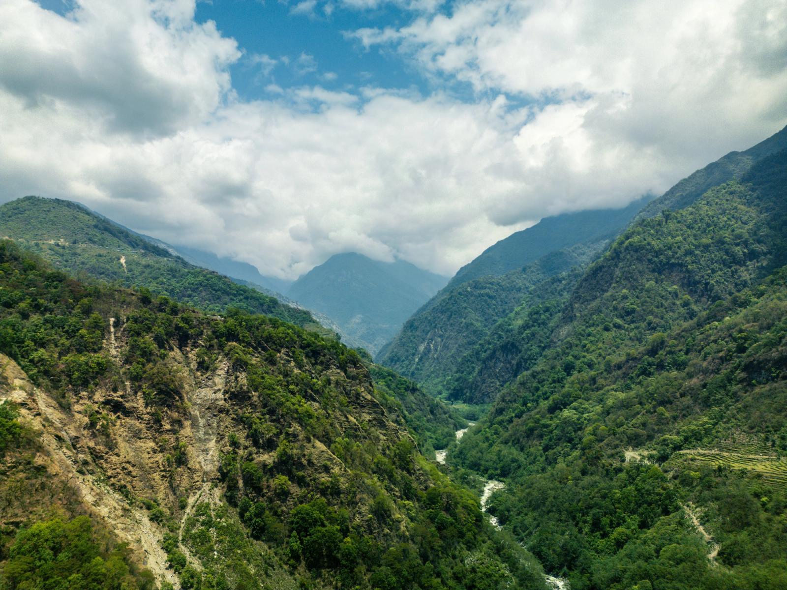Lush green valley in Ghandruk with mountains and river under a cloudy sky in Nepal
