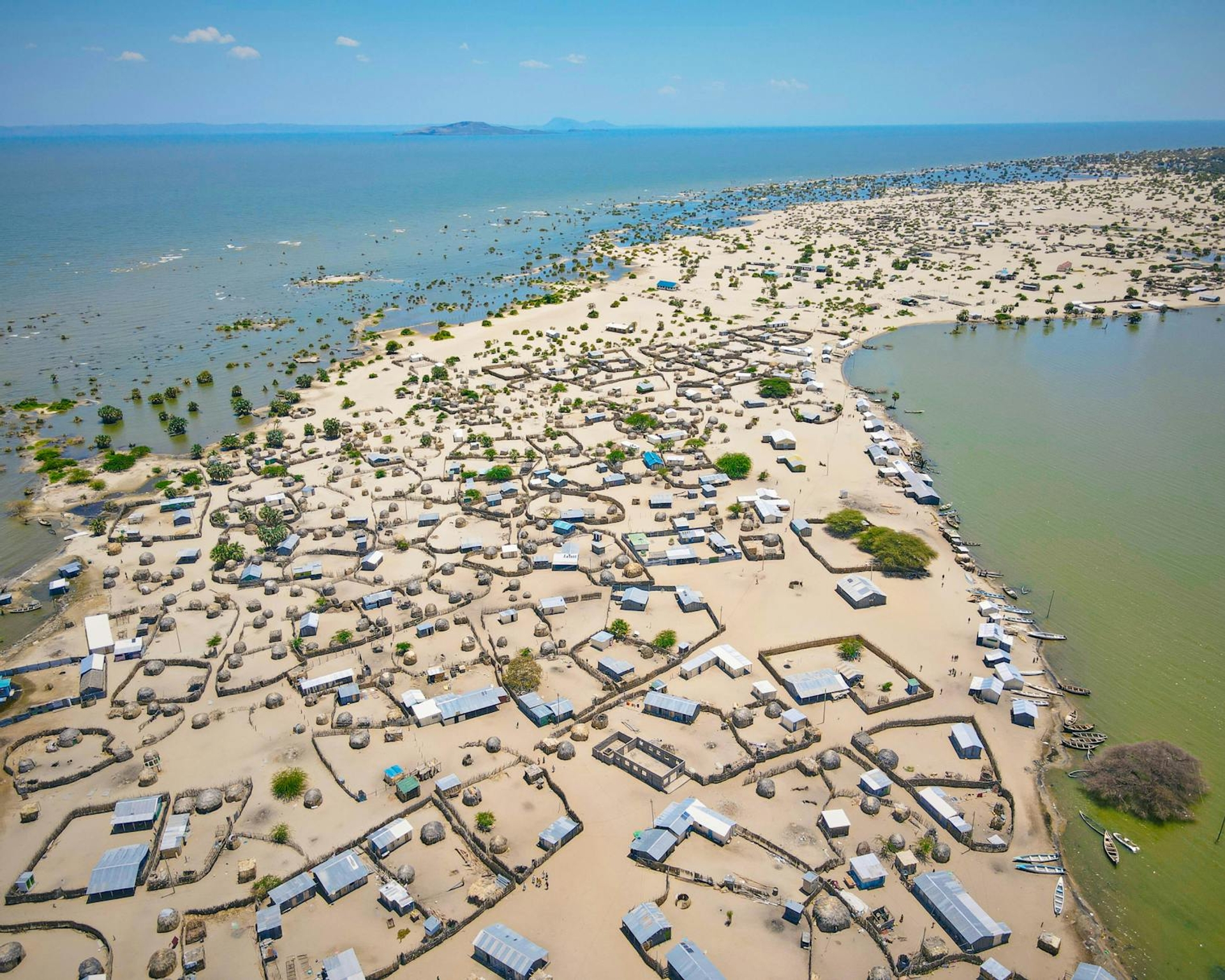 An aerial view of a dense lakeside fishing village on a sandy spit