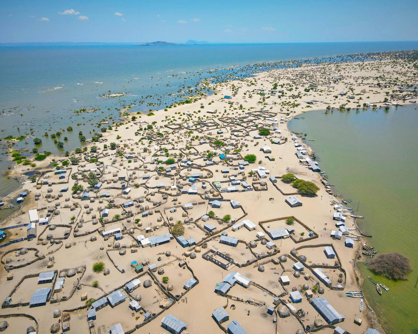 An aerial view of a dense lakeside fishing village on a sandy spit