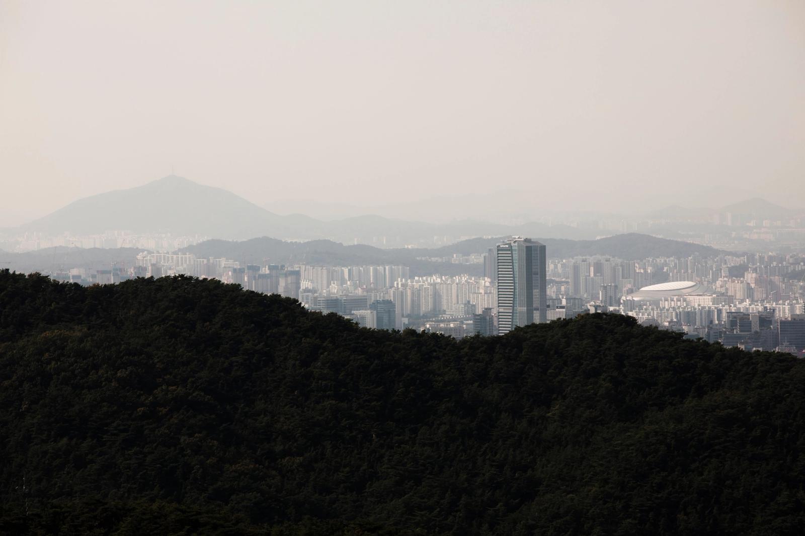 Aerial skyline of Seoul from forested hillsides, featuring distant mountains